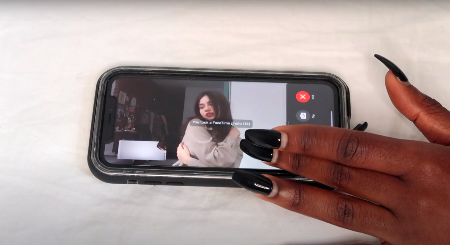 Phone screen showing a model posing during a FaceTime call while another person takes a screenshot.