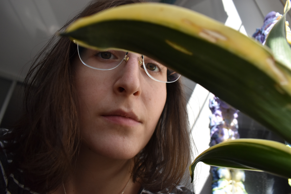Leah stares into the camera behind her dying snake plant.
